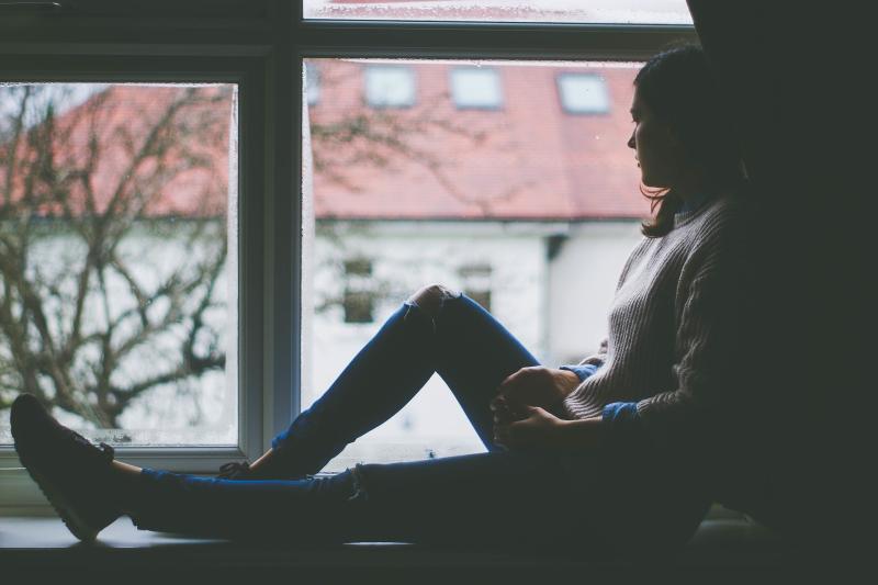 Young woman sitting on a windowsill staring out 