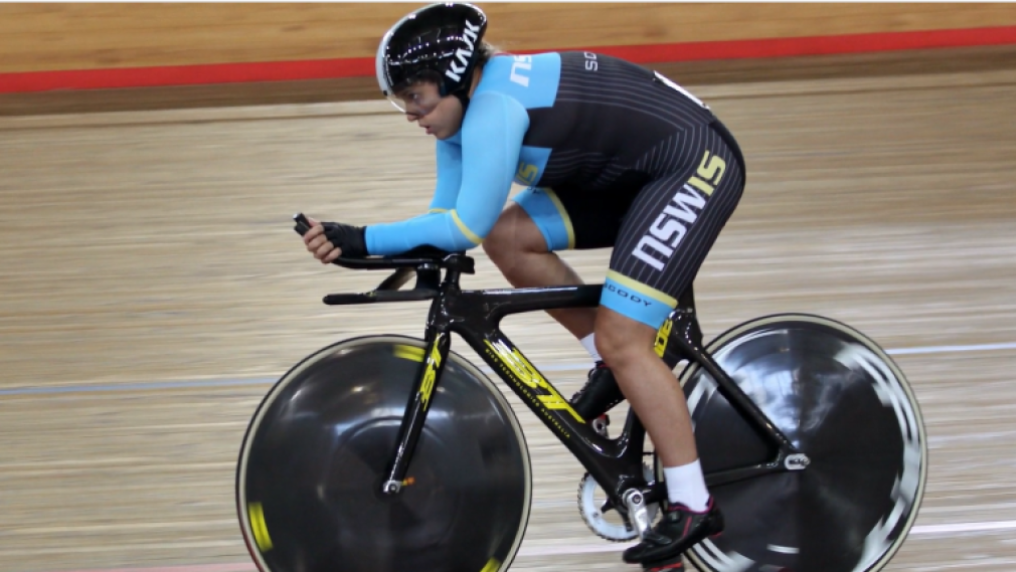 Female athlete cycles on indoor track, in professional cycling gear