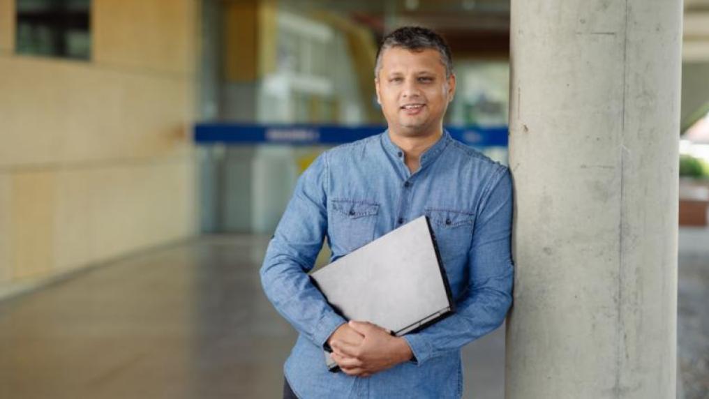 student leaning against a column, relaxed, holding laptop