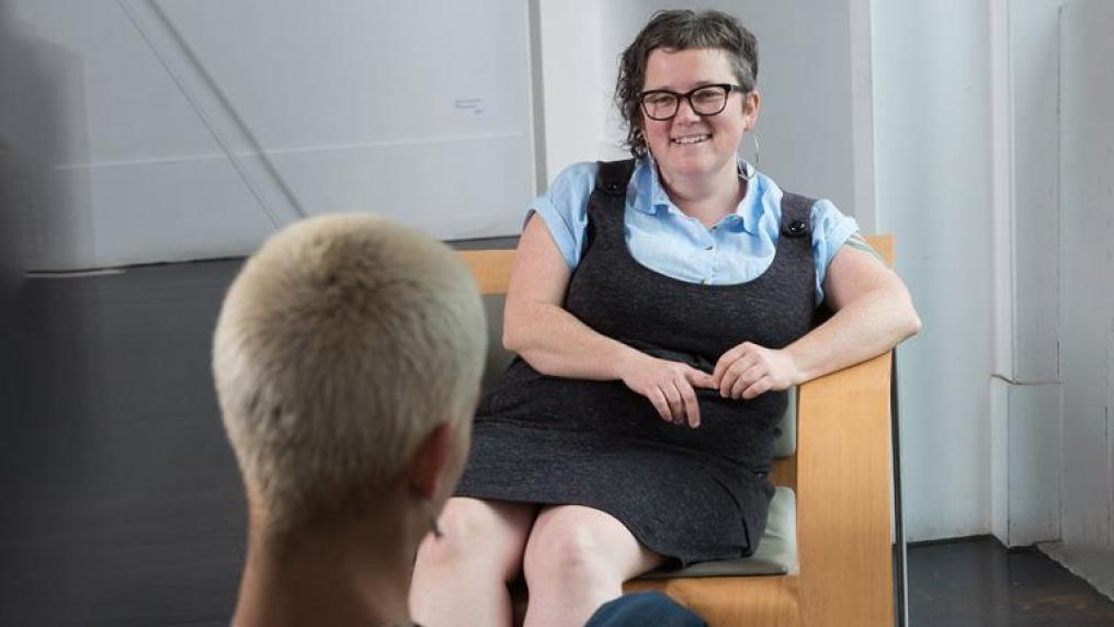 A woman sits opposite another woman, smiling and listening