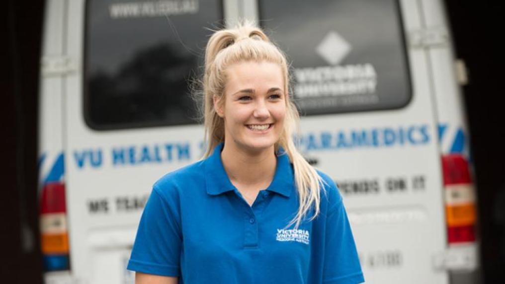 A VU emergency health care student in front of an ambulance.