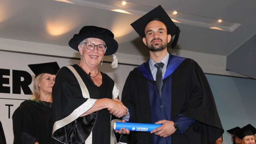 undergraduate receiving his testamur and shaking hands on stage at graduation ceremony