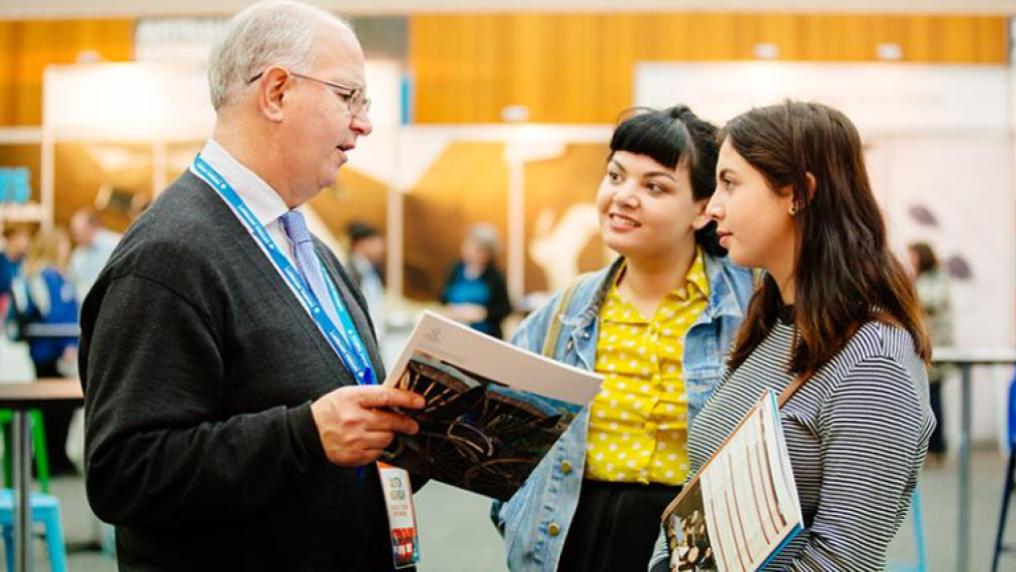 two female students talk to staff members on open day