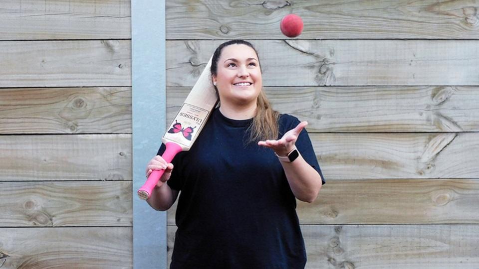 Rachel Webb (née Napolitano) holding a cricket bat over her shoulder, and throwing a cricket ball in the air