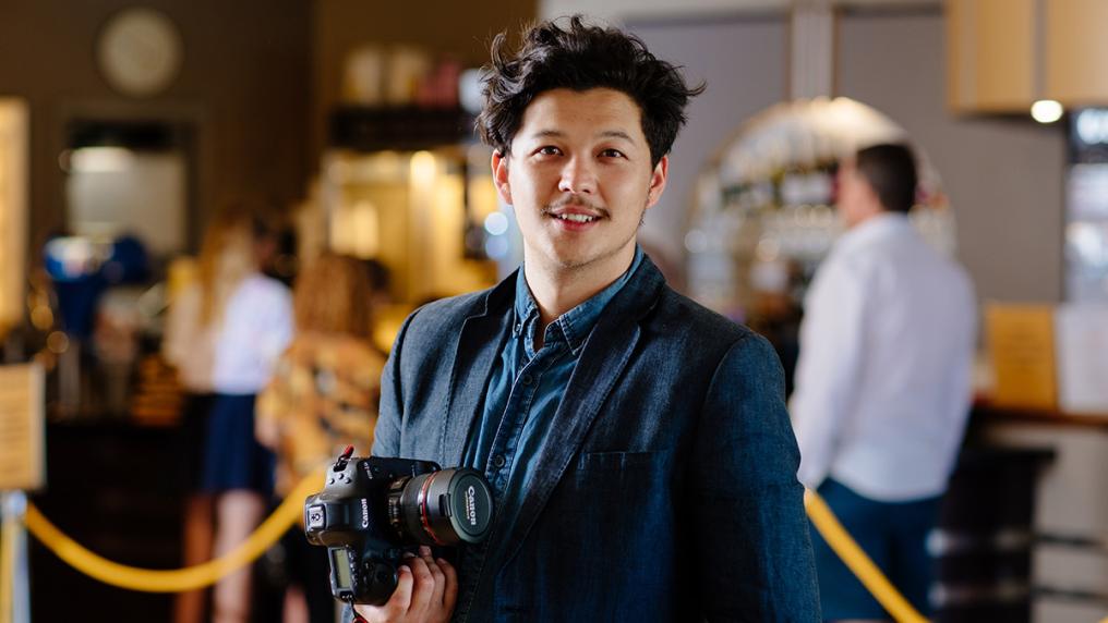 Young, well-dressed man holds camera at cinema foyer