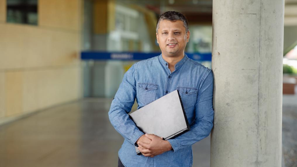 Middle-aged man in professional clothing, holding laptop on campus