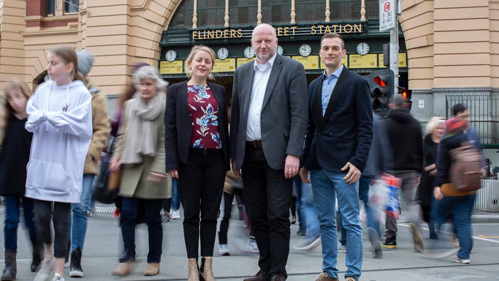 3 professional-looking researchers on a busy street in front of Flinders Street Station