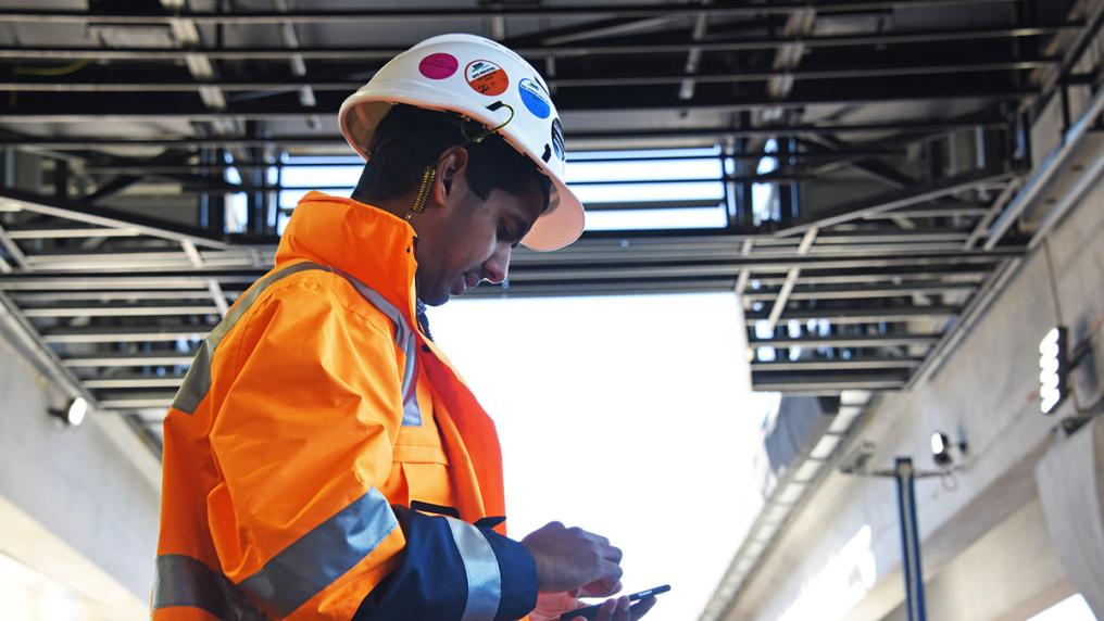 South Asian man in bright orange work uniform and hard had, at train contruction site
