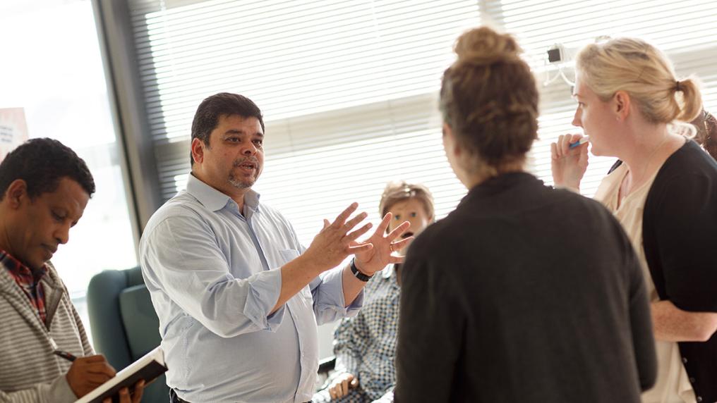 teacher with adult students using dummy to demonstrate healthcare techniques