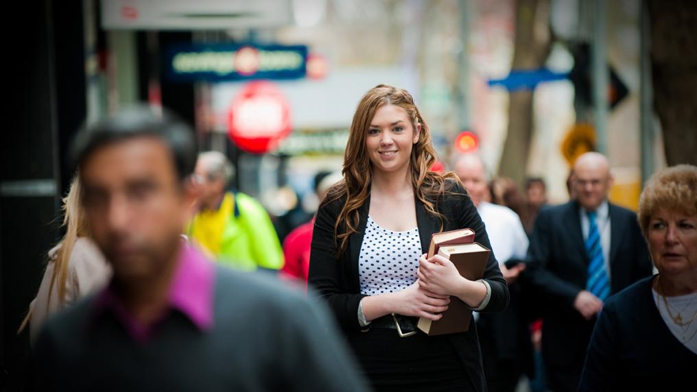 Young white woman on busy city street, holding law books in professional clothing, smiling at camera