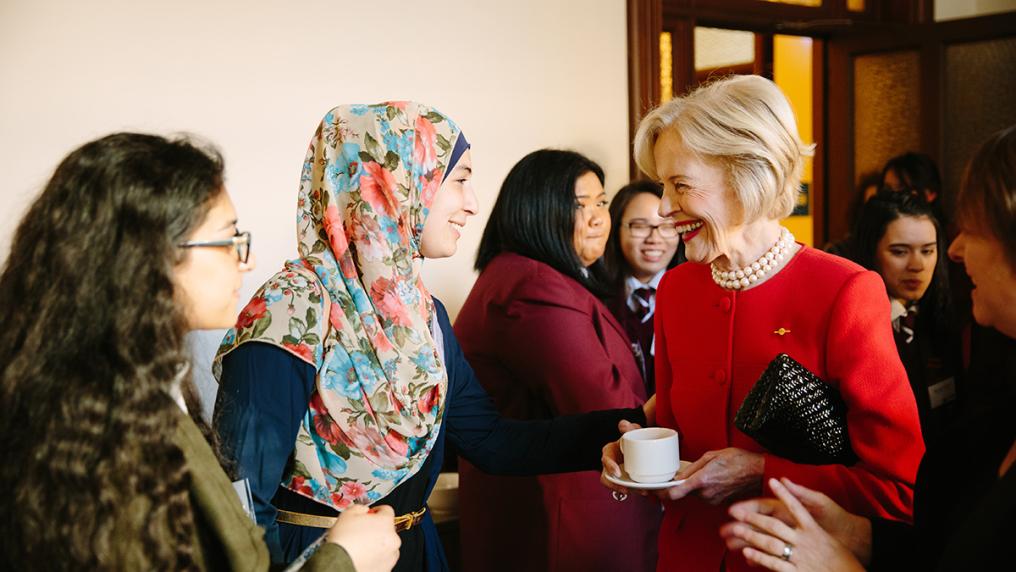 Sophisticated older woman in a red suit and pearls speaks to multicultural group of younger women