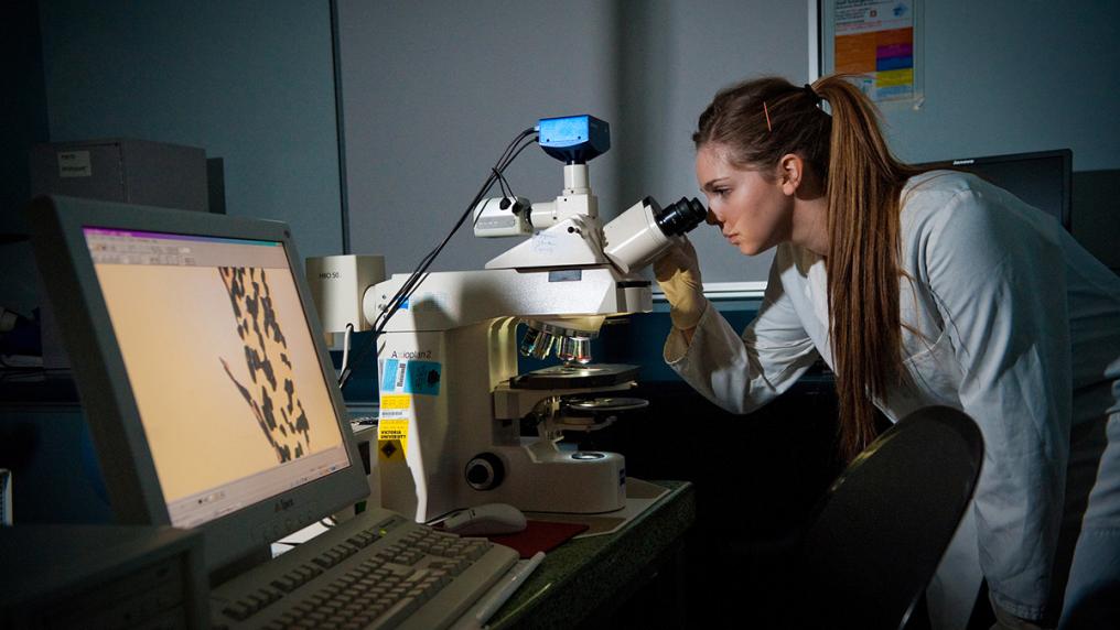 Woman in a lab coat looking into a microscope