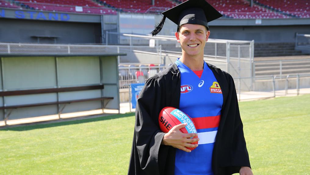 Man in AFL Western Bulldogs football uniform and graduation gown and capon sport ground