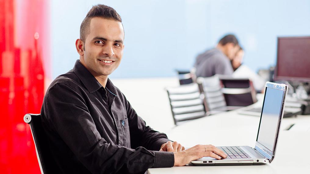 Student smiling at camera, while working on a laptop.