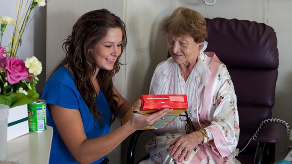 A VU student kneels alongside an elderly woman seated in a chair as she shows her something and they look at it together