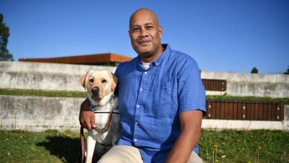 Polynesian man, dressed professionally, in an outdoor setting with a Labrador