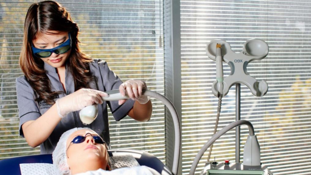 VU student standing over a patient applying a dermal therapy to her face with a device