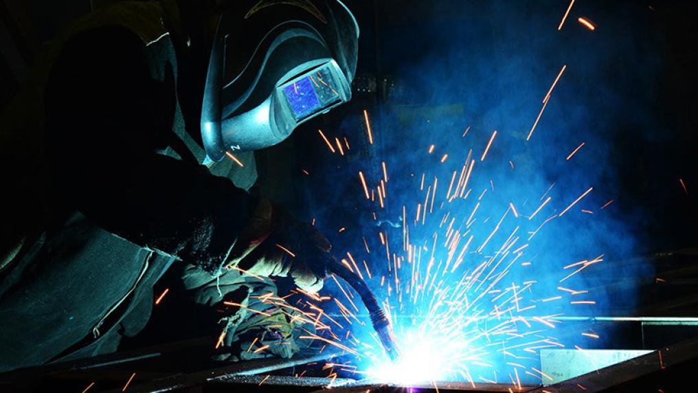 Student welding, in protective gear with sparks flying