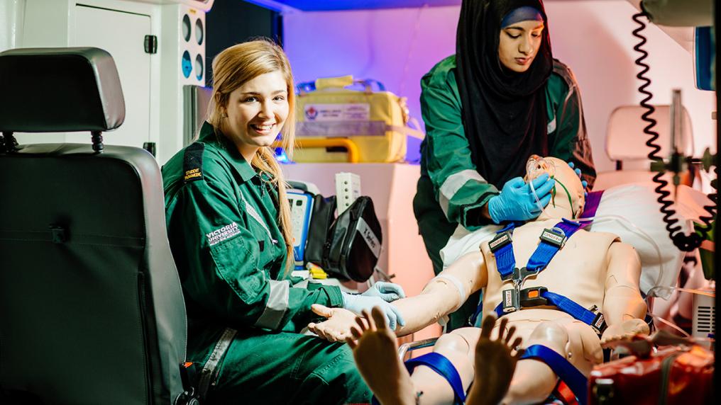 Paramedicine students in uniform learn in a simulated ambulance environment