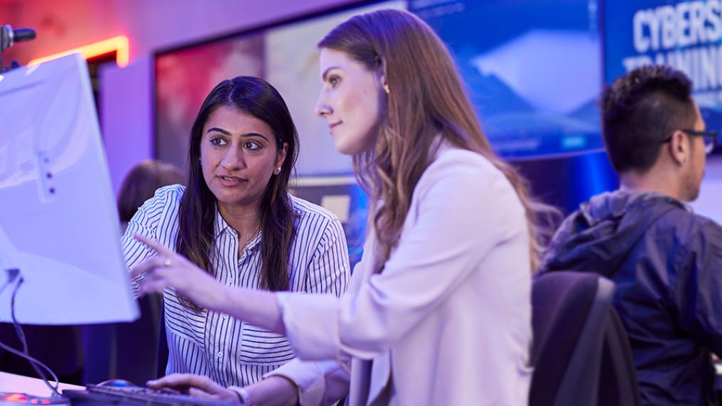 two female students intently looking at a computer screen together, in the CyberSecurity Training Centre