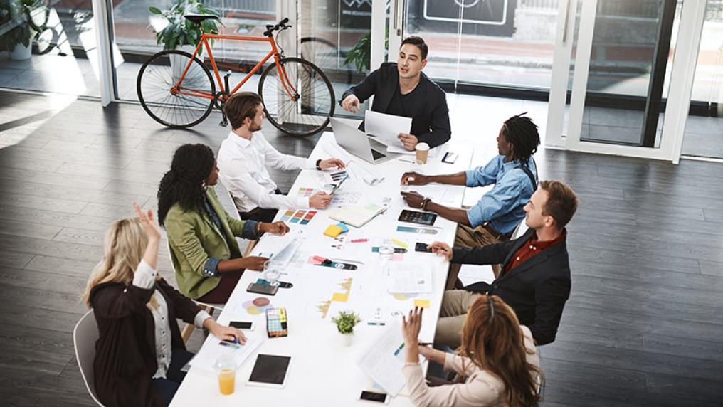 A project manager assigns tasks to workers sitting around a table.