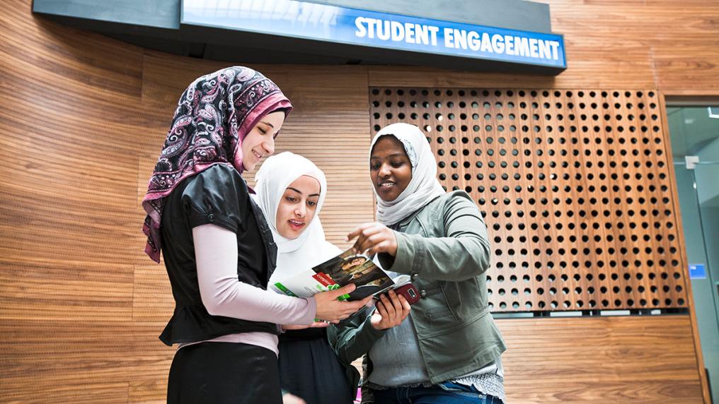 Three students wearing hijabs talk together on campus.