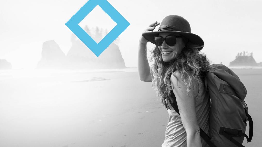 A student wearing a hat and backpack walks across a beach, with the VU blue branded diamond in the background.