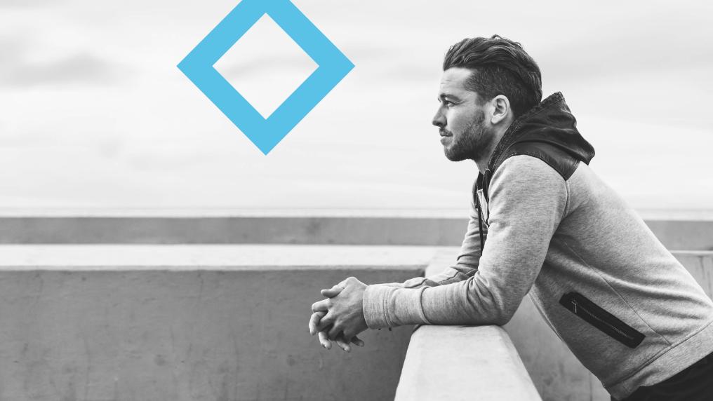 A student leans over a fence, staring out into the distance, next to the VU blue branded diamond.