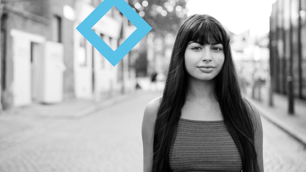 A student stands in the middle of a residential street, next to the VU blue branded diamond.