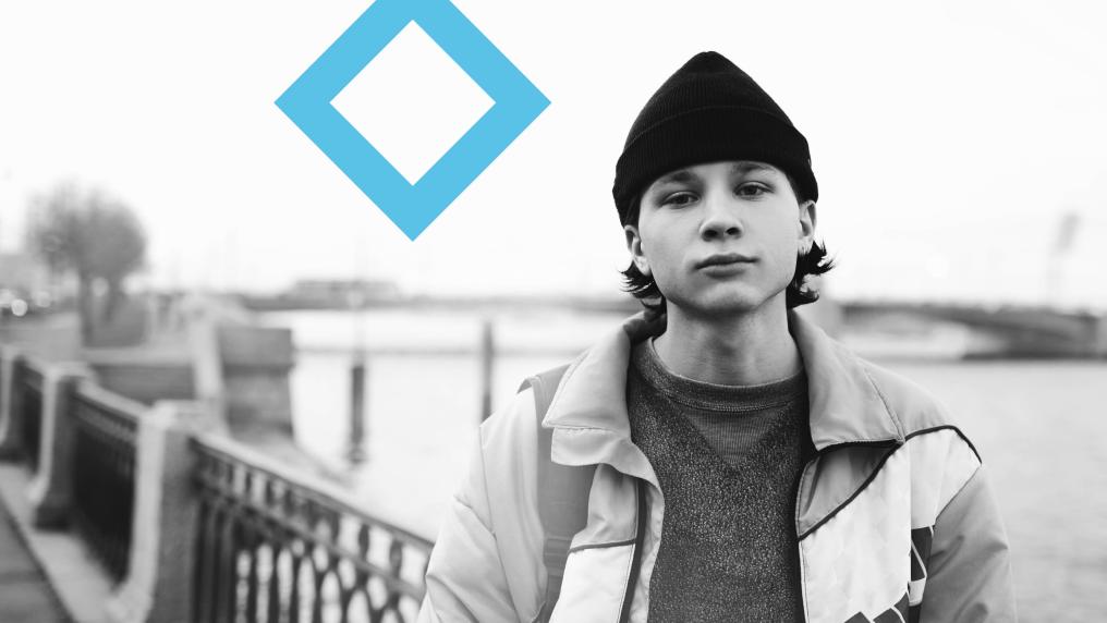 A student in a beanie and jacket stands on a bridge, with the VU branded blue diamond in the background.