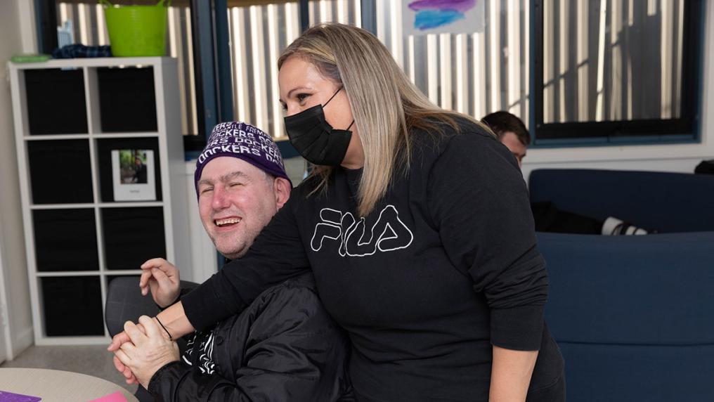 A smiling man with a disability interacts with a young female care worker
