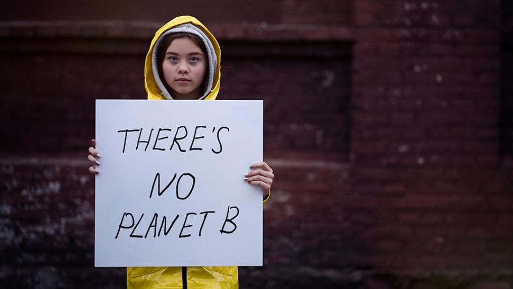 A young girl in a yellow raincoat holds a sign reading 'There's no planet b'