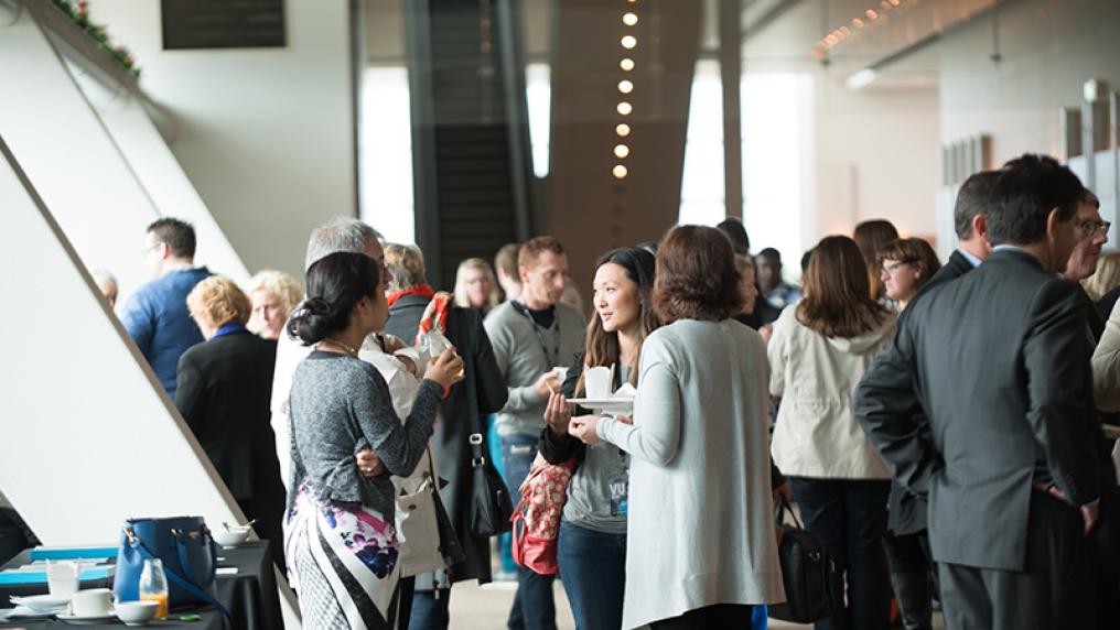 A group of professional-looking men and women talk in groups in a large, modern foyer