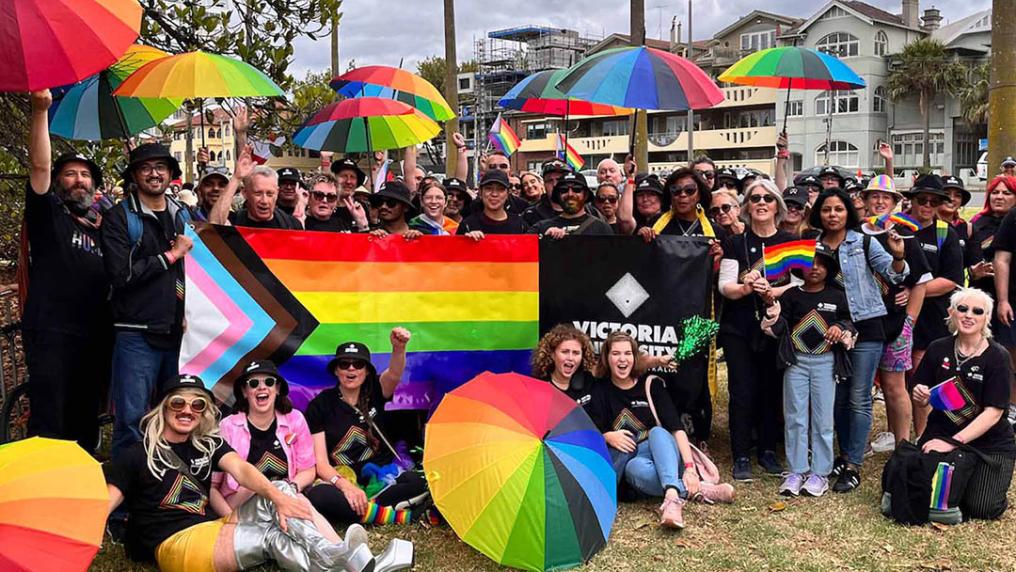 VU staff and students gather together at Pride March, holding the Pride flag and rainbow umbrellas.