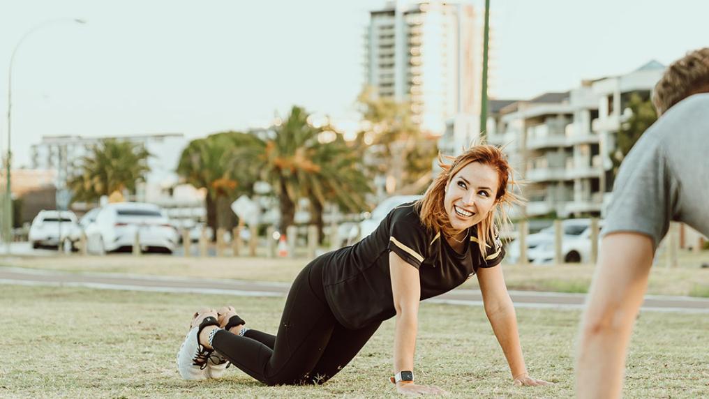 A woman doing push ups on grass outside.
