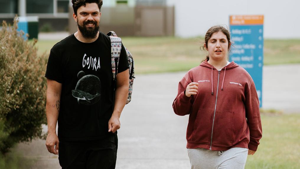 A young man walks outside with a woman who appears to have disability