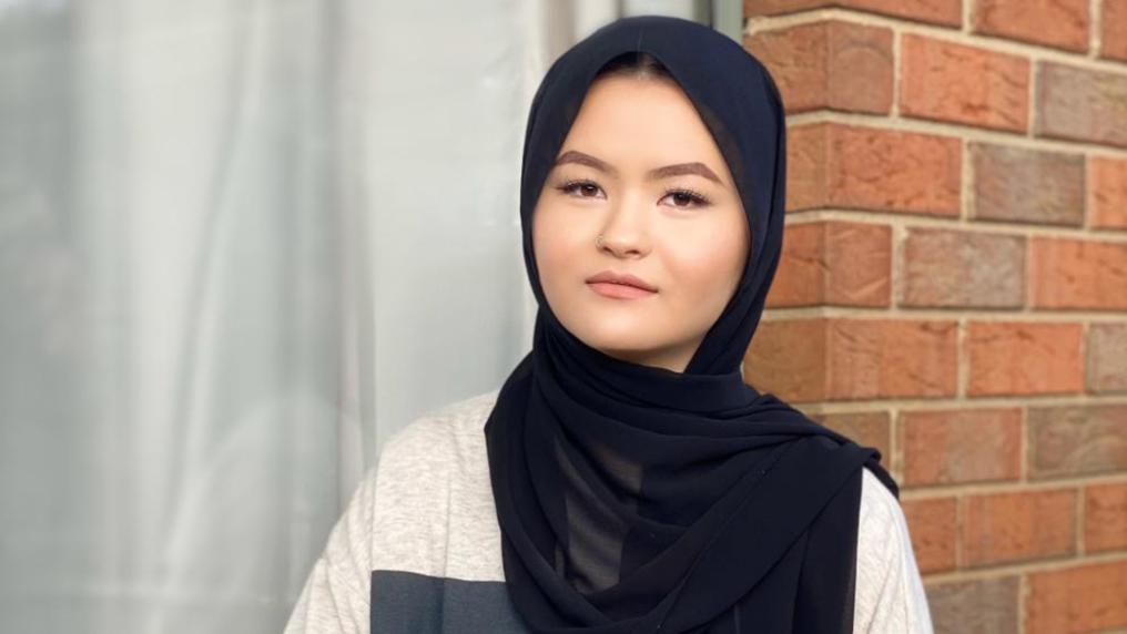 A young woman in a hijab poses outside a brick building