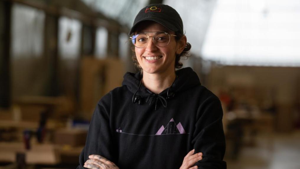 Kyriaky smiling at the camera, standing in an empty carpentry studio