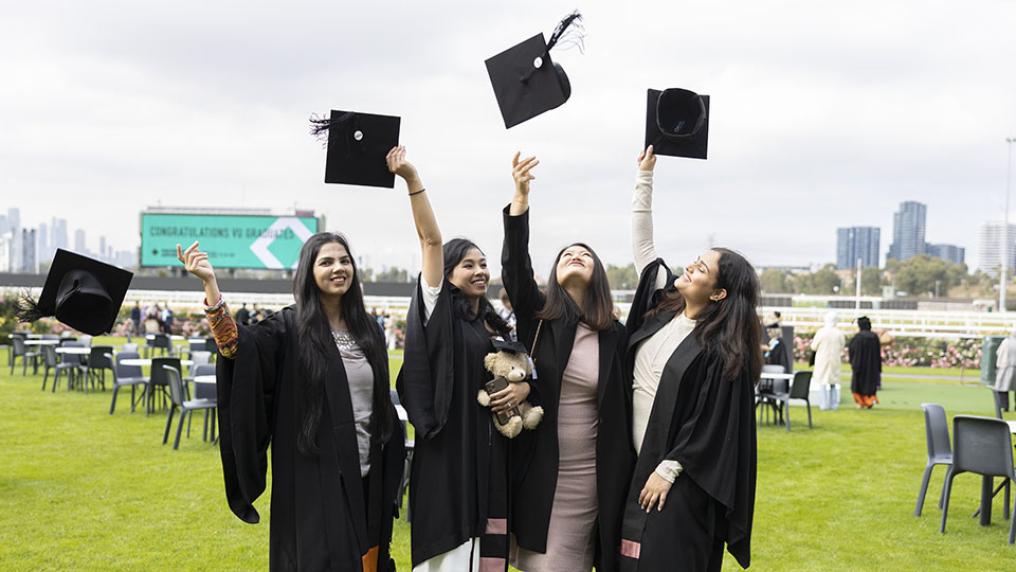 A group of four graduates throw their hats in the air.