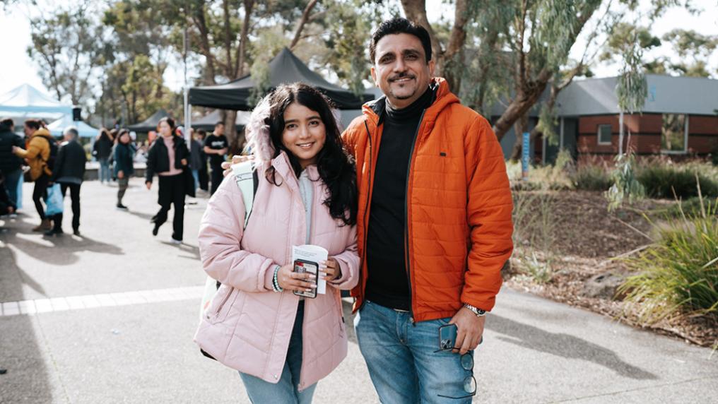 A man and younger woman who look like father and daughter outdoors with stalls in the background
