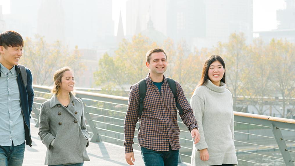 Four international students crossing bridge over Yarra River in Melbourne CBD.