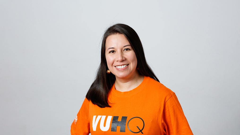A smiling woman wears an orange t-shirt that reads VUHQ