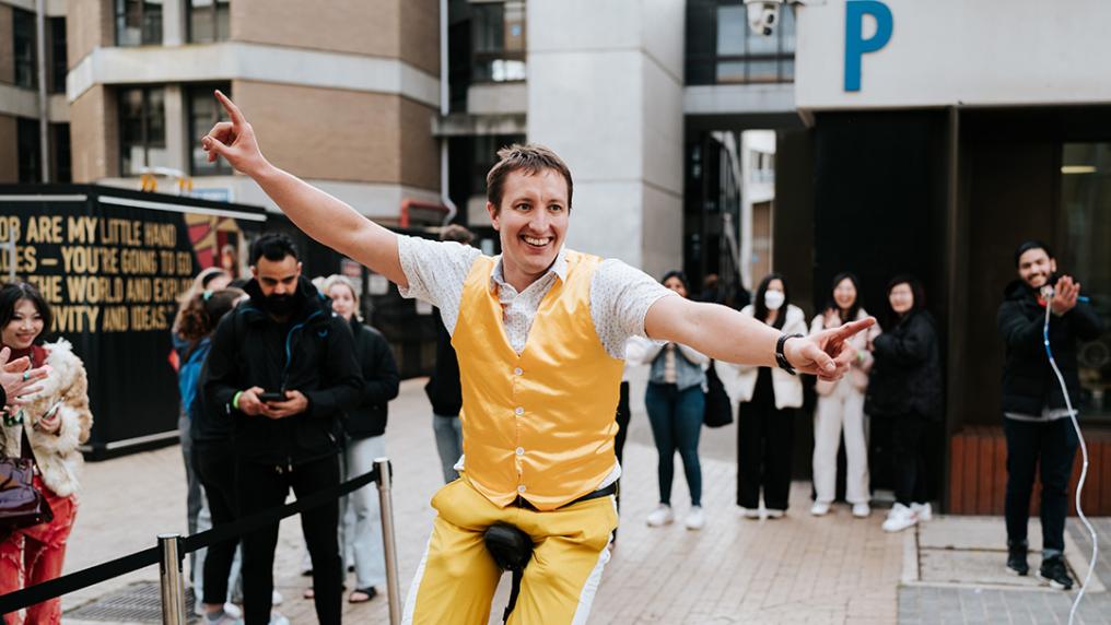 A man in yellow riding a unicycle in front of a crowd in a university courtyard
