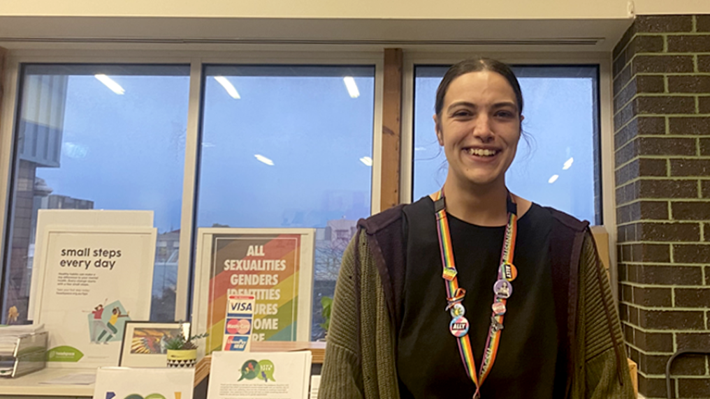 Briahny Lundberg standing at her desk at headspace Sunshine, smiling at the camera. There are framed posters and a window in the background.