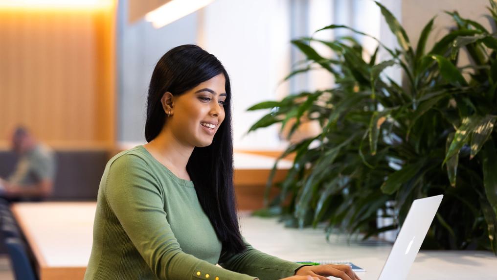 A student sits at a bench on a laptop.