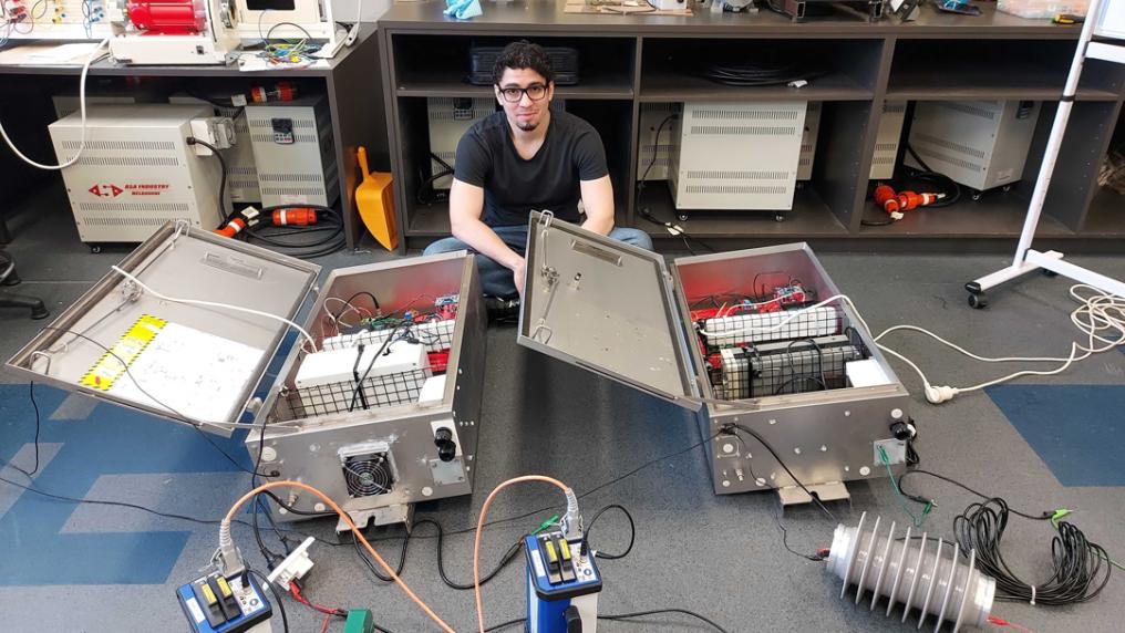 A man sits on the floor of a lab surrounded by electronic gear