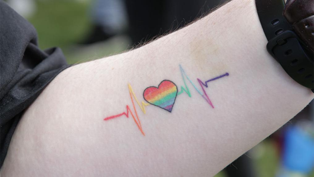 Tattoo of a rainbow heart on a forearm.