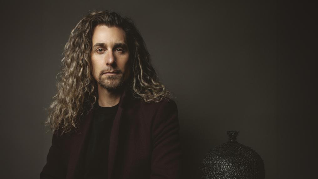 A person with long curls and a goatee beard poses for the camera