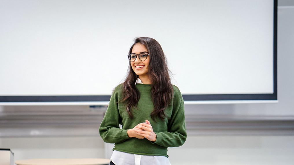 A student in glasses giving a presentation in a classroom.