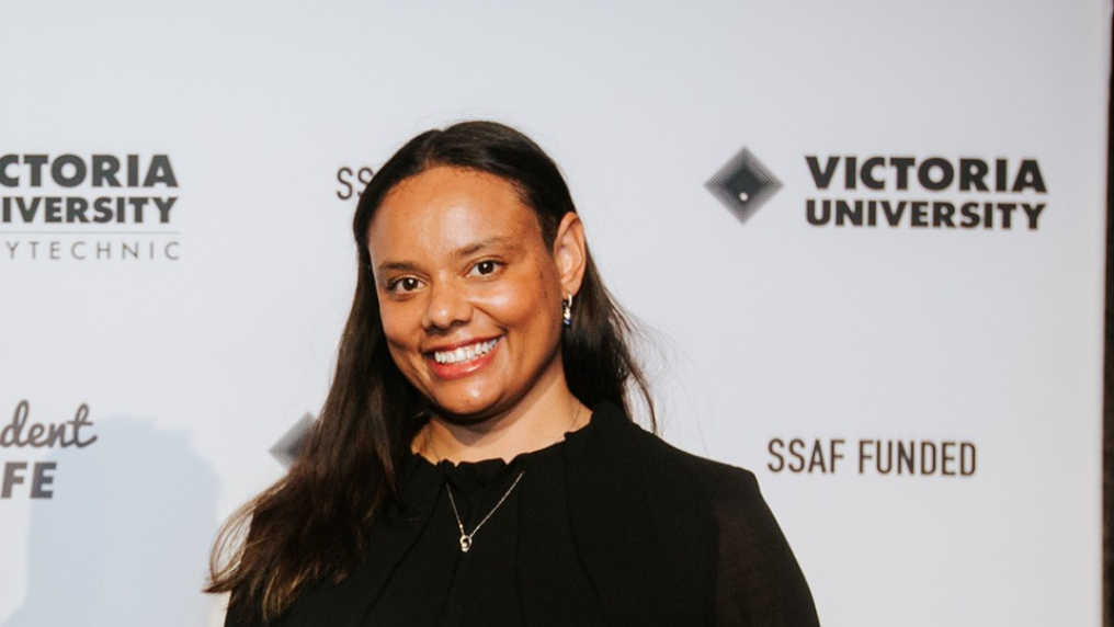Tahnee Towers at 2023 Student Leadership Awards. Tahnee is standing in front of a VU-branded media wall and smiling at the camera.